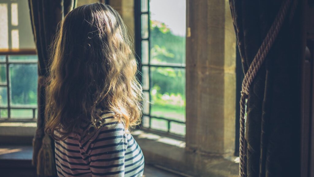 窓辺で静かに立ち止まり、自分の選択を振り返る女性の後ろ姿