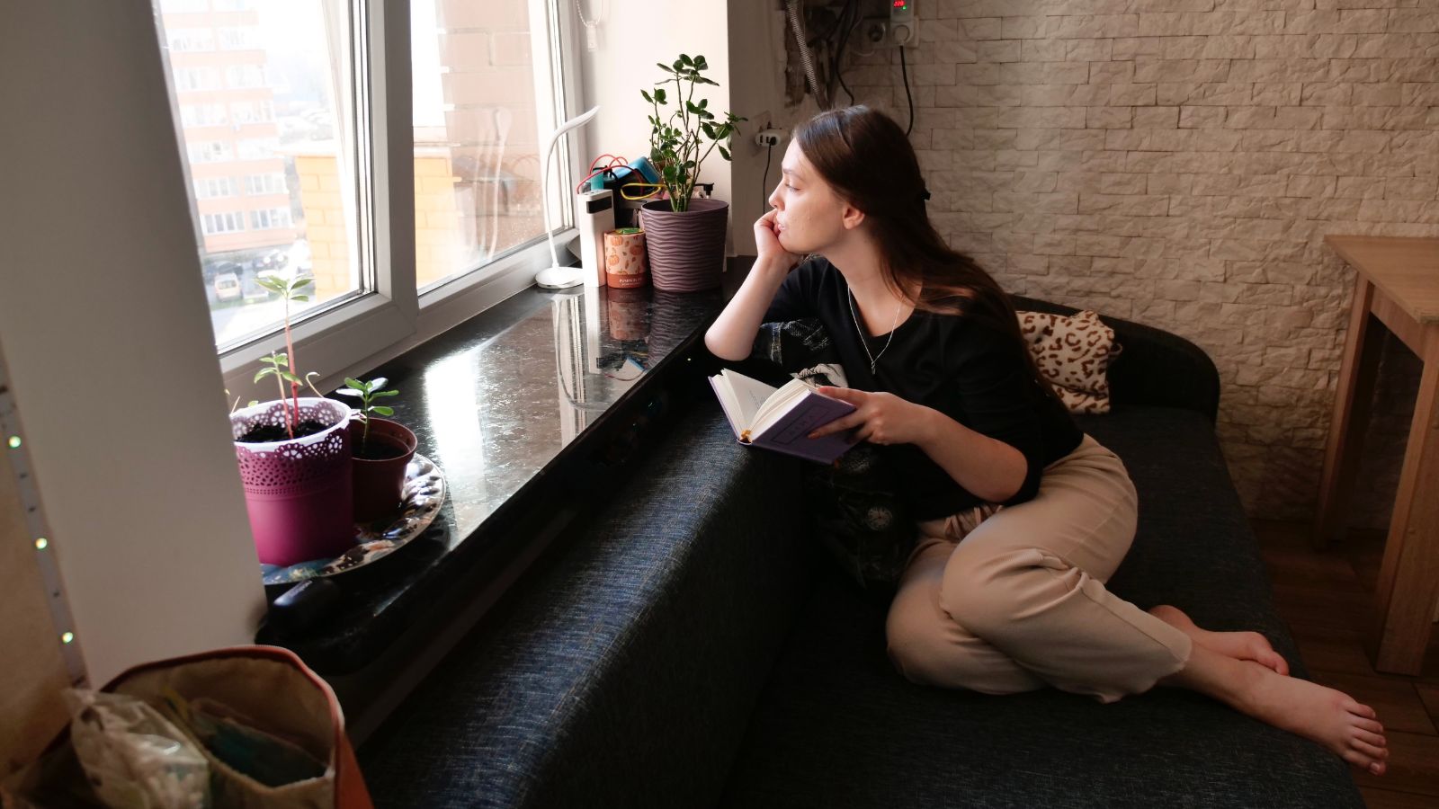 窓辺で本を持ち、人生の選択について考え込む女性